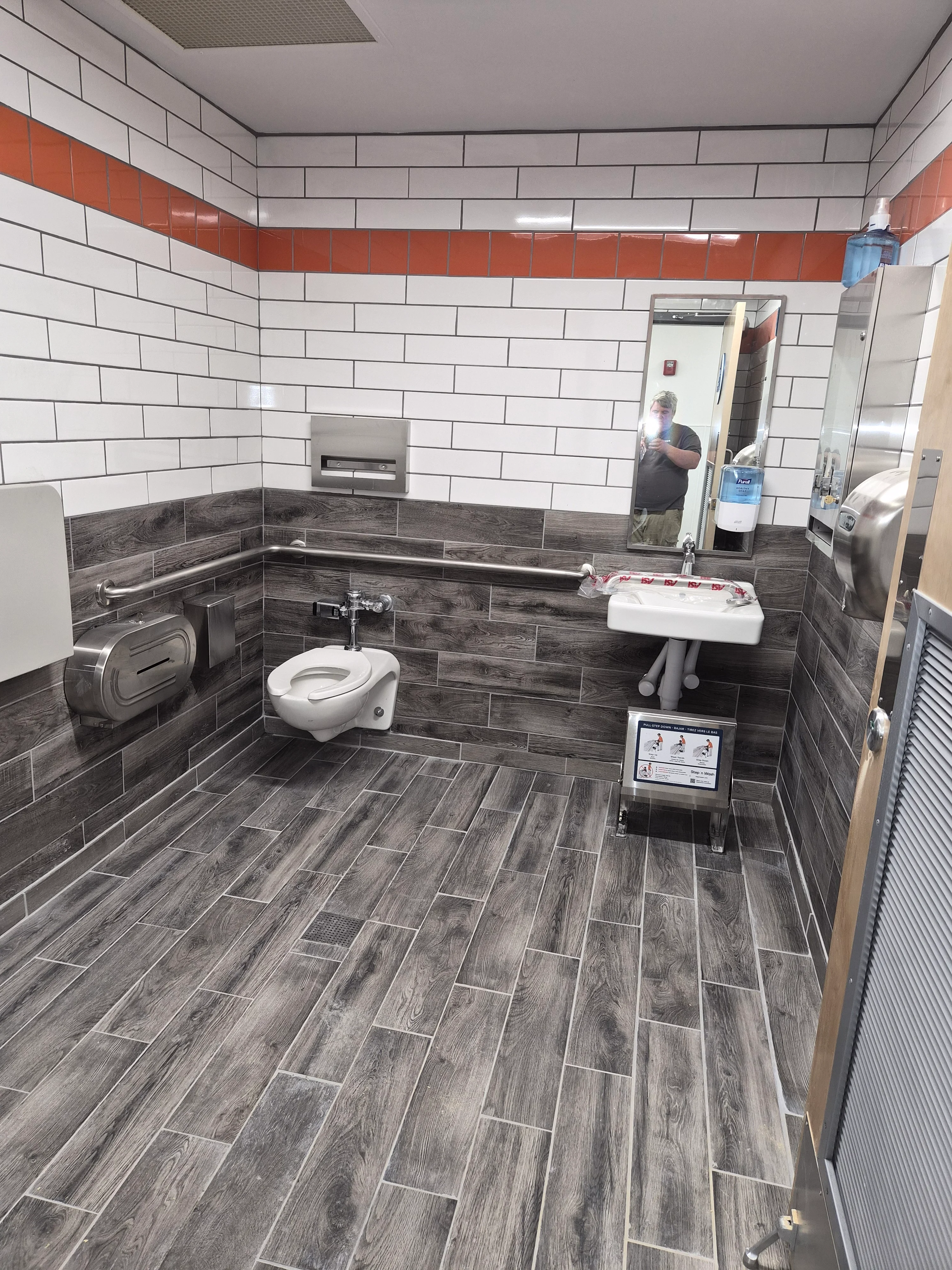 Modern commercial bathroom with wood-look tile flooring and white subway tile walls