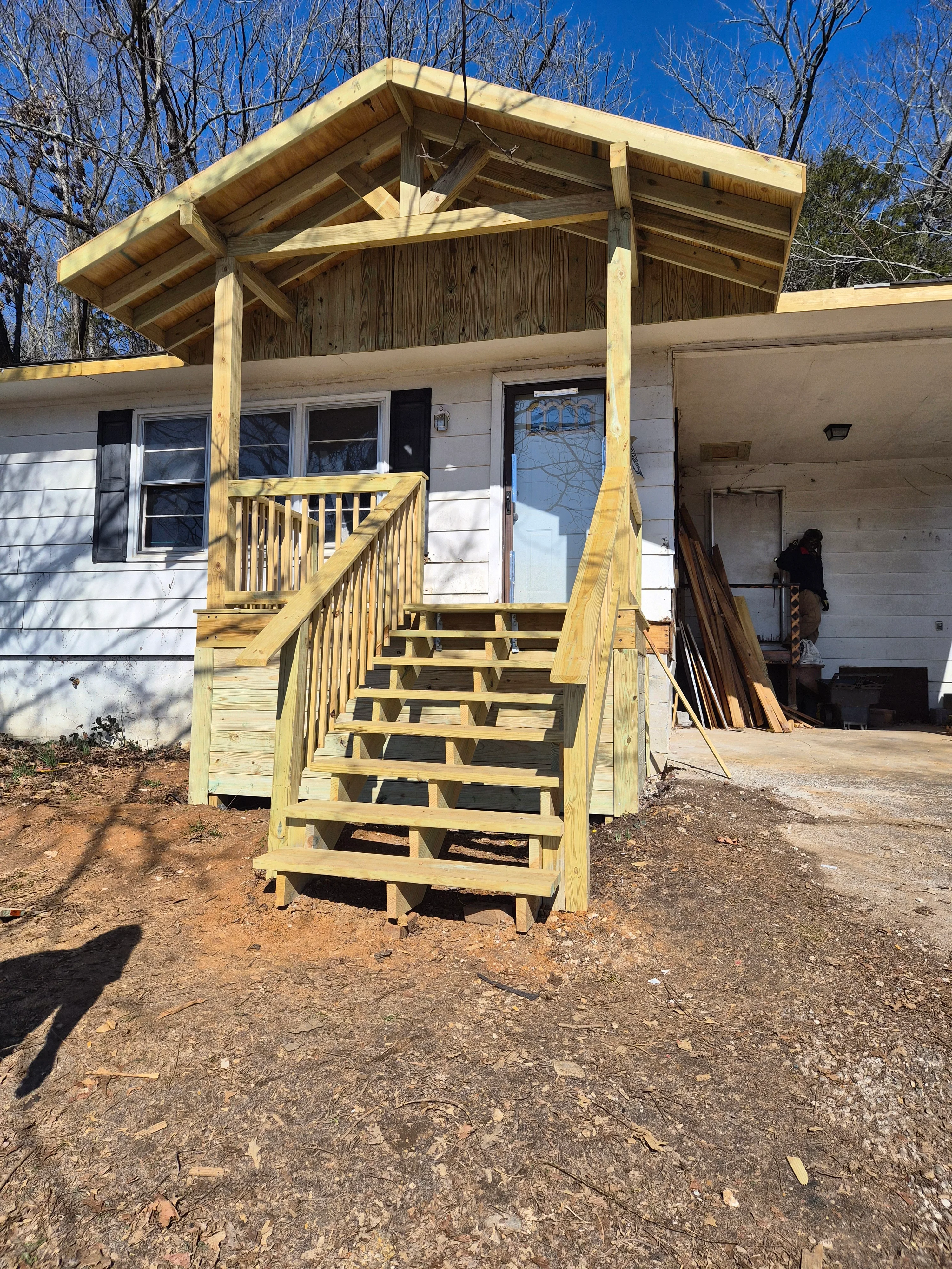 New wooden front porch with gabled roof, stairs, and railings on residential home