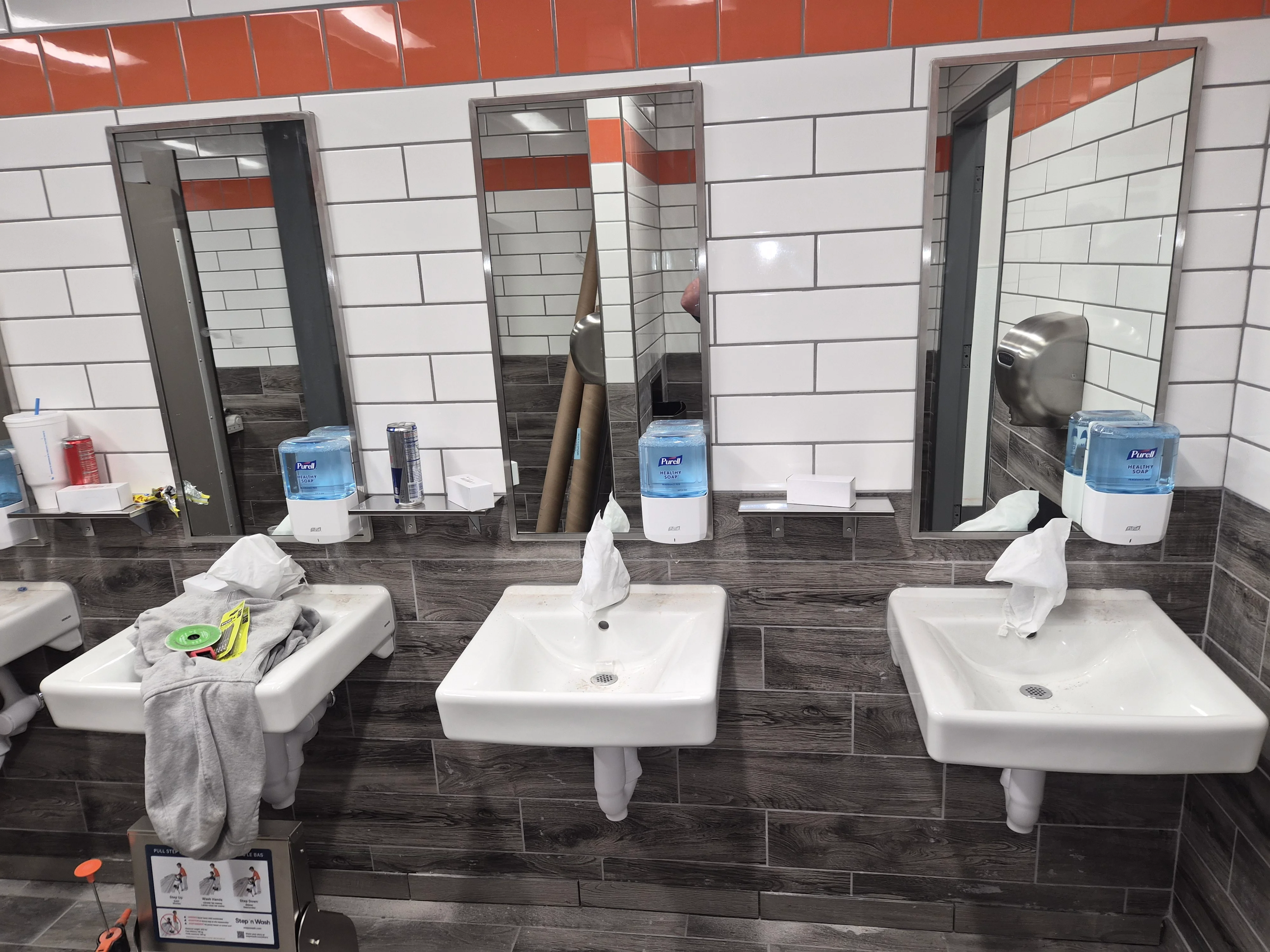 Commercial bathroom with three white pedestal sinks, dark tile flooring, and white subway tile walls