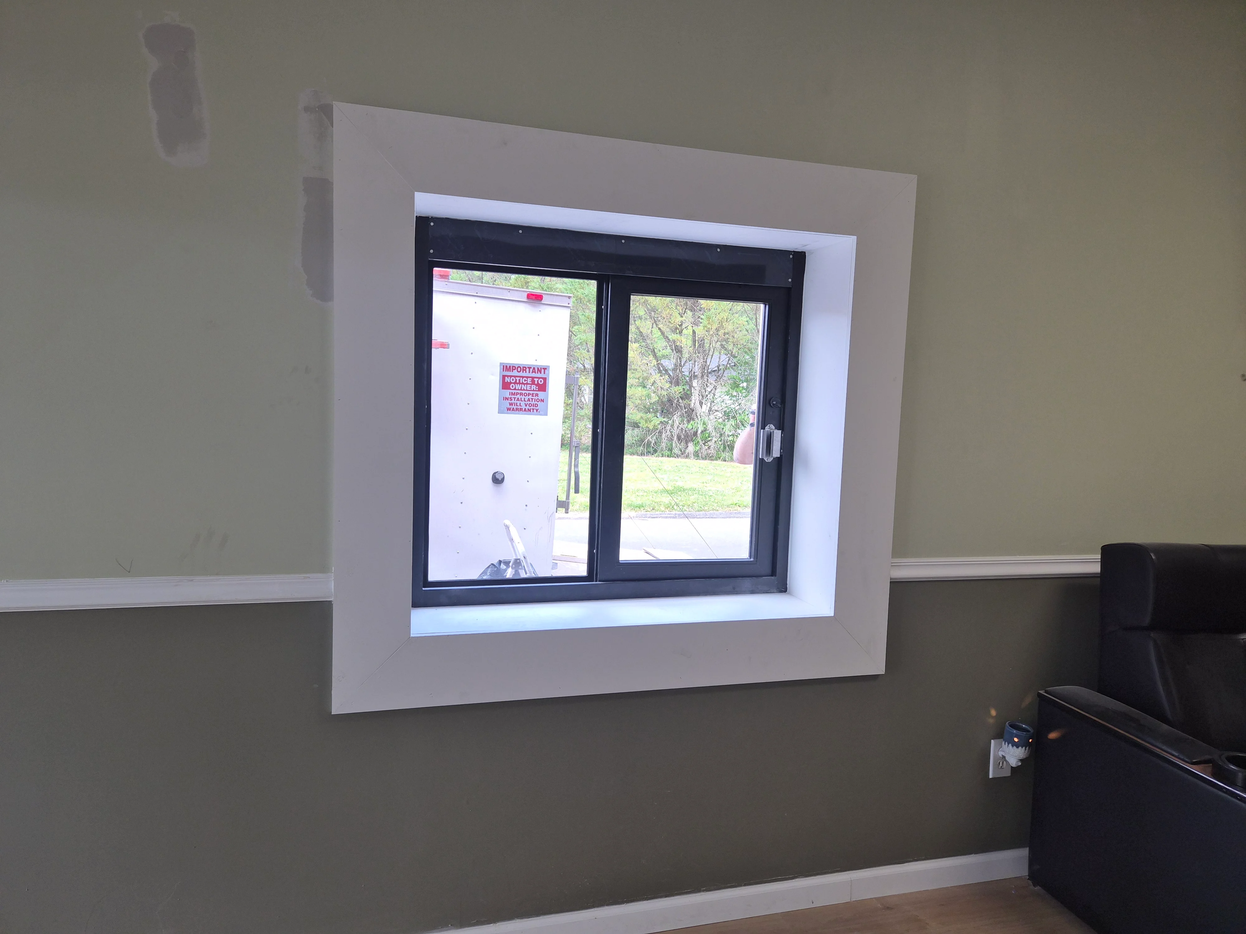 Black-framed sliding window installed in white drywall opening with finished trim